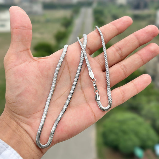 Silver snake chain necklace held in a hand with a blurred outdoor background