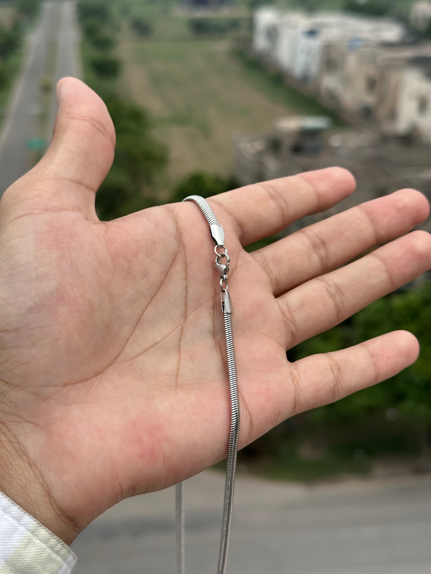 Hand wearing a silver chain necklace with a blurred background