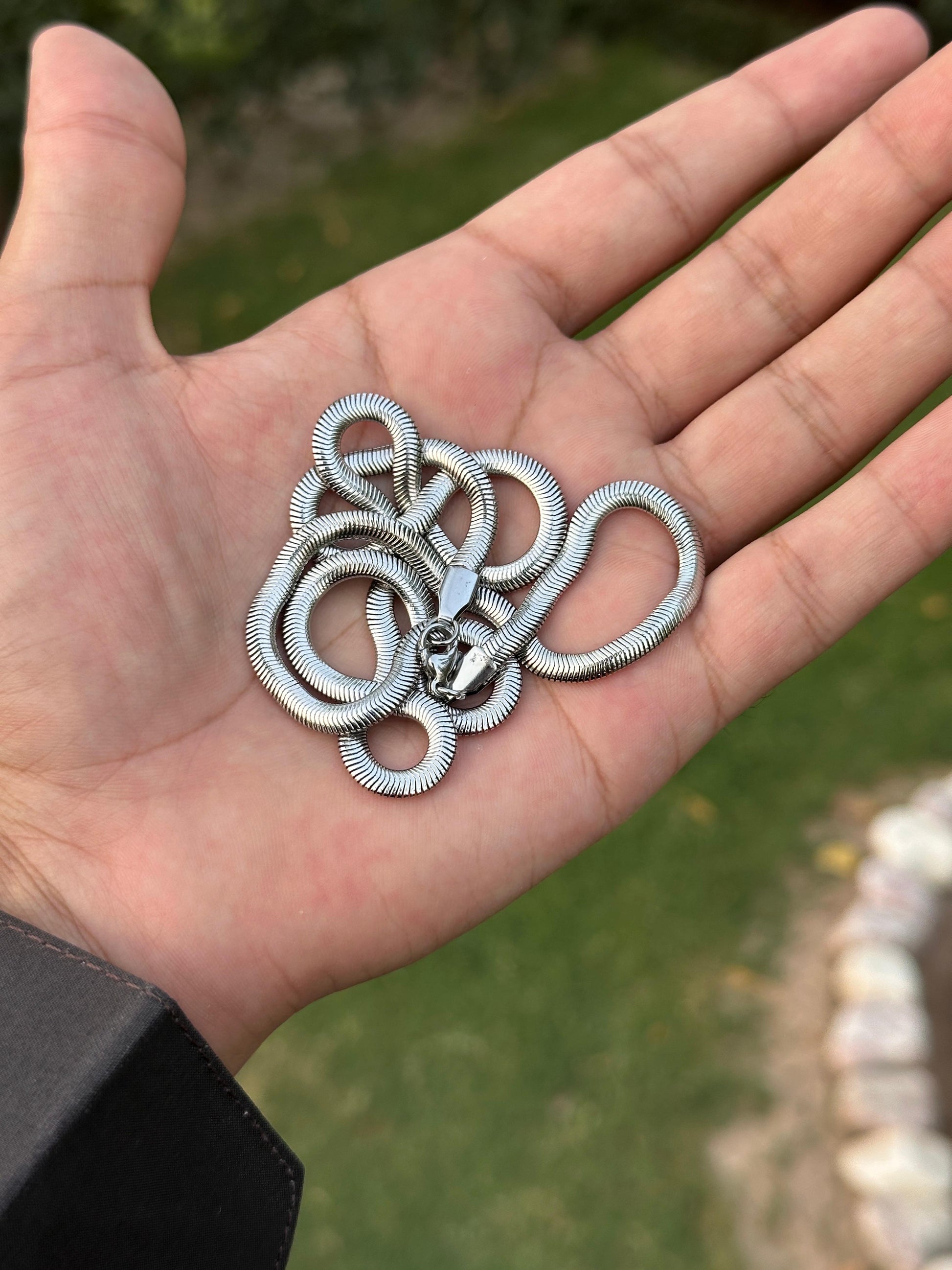 Hand holding a silver necklace with a blurred green background